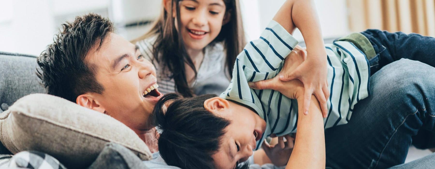 father plays on a couch with his young children